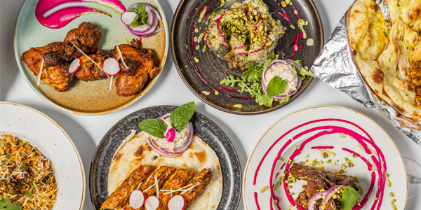 Overhead view of a vibrant spread of Indian fusion dishes at Rasa Palladium – RestoBar, featuring naan, grilled meats, rice dishes, and colourful garnishes with artistic drizzles of sauce, presented on elegant plates.
